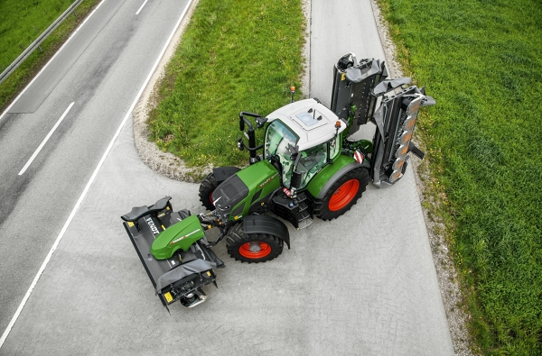 Fendt 600 Vario El tractor Fendt 600 Vario verde con llantas rojas e implemento cerrado circula con un radio de giro pequeño en una carretera gris.