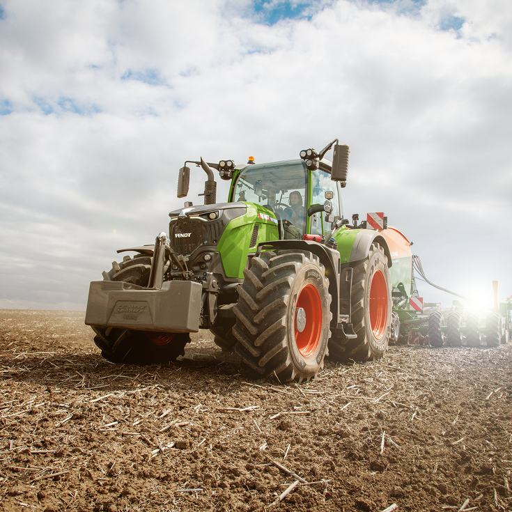 Un tractor Fendt con las características llantas rojas circula por un campo. Se puede ver el cielo nublado al fondo.