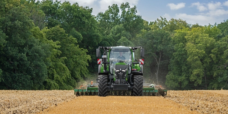 Un Fendt 620 Vario verde en el campo durante el laboreo con el bosque de fondo
