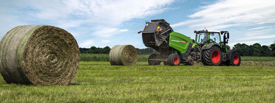 Rotoempacadora Fendt Rotana V En el horizonte un tractor Fendt circula por un campo con una rotoempacadora Fendt Rotana V enganchada, delante dos pacas redondas prensadas