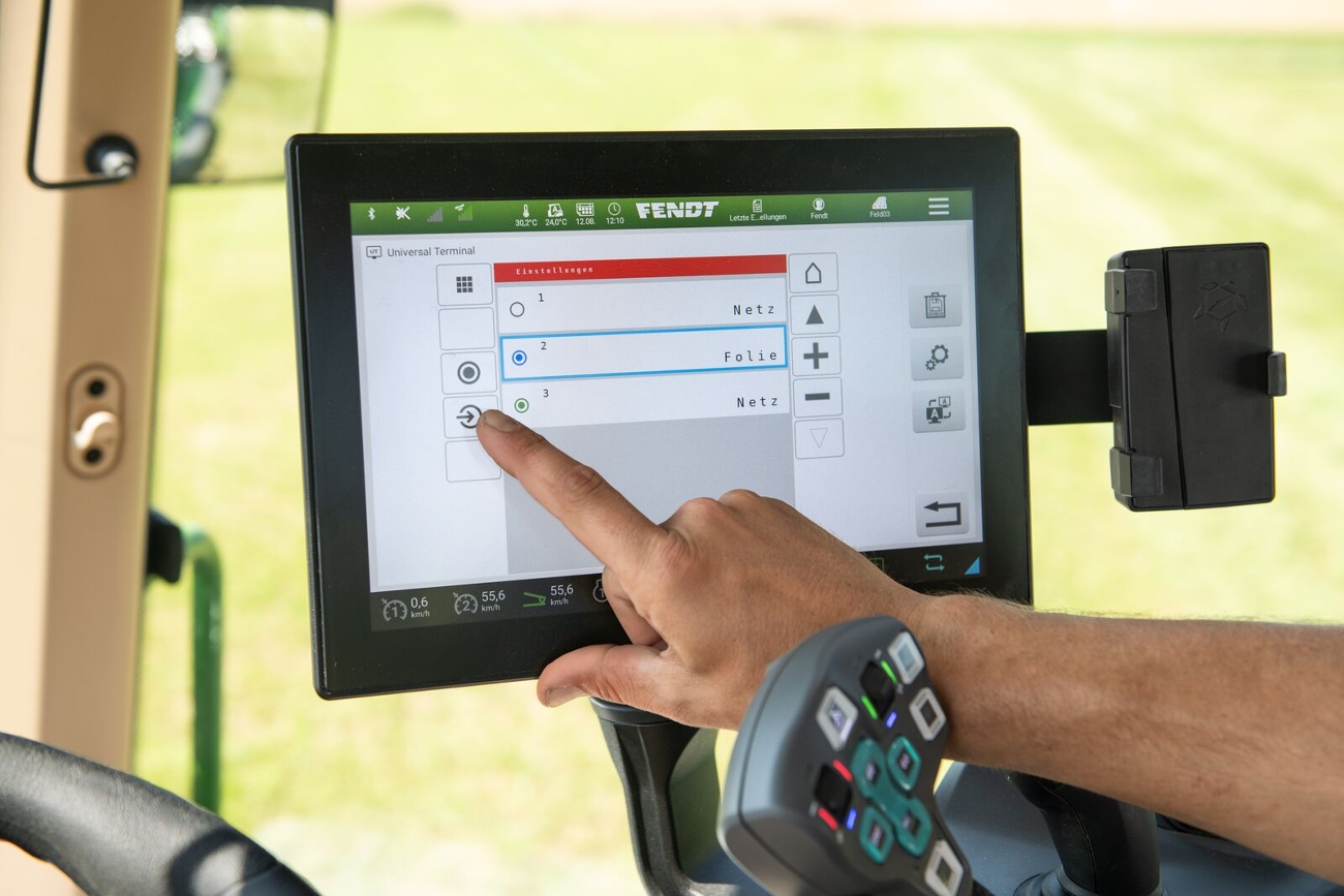 Control del almacén de rollos de las empacadoras Fendt Rotana Combi directamente desde la cabina del tractor Vista de la cabina del tractor hacia el terminal situado en el reposabrazos, que muestra las funciones de la rotoempacadora.