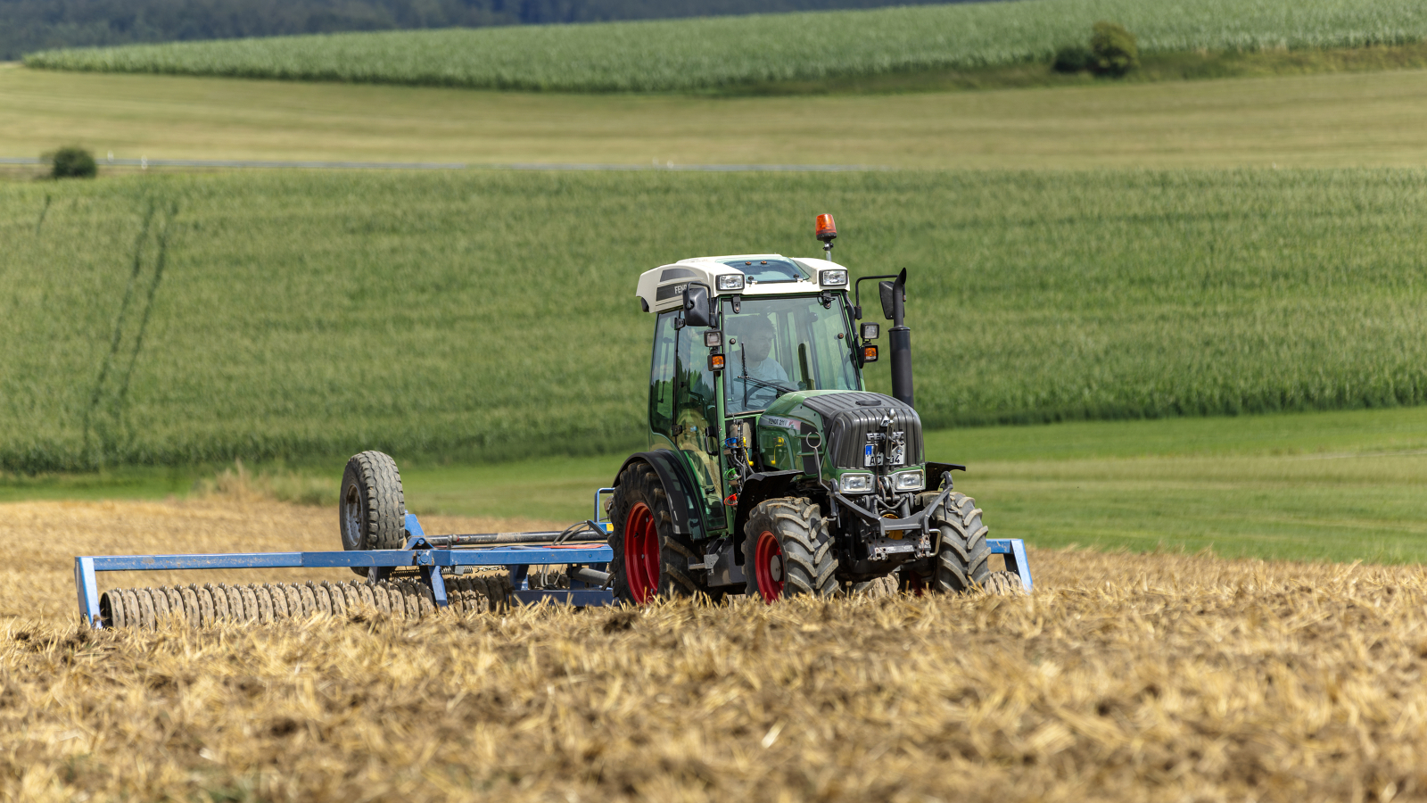 Un agricultor conduce por un campo un pequeño Fendt 200 V Vario.