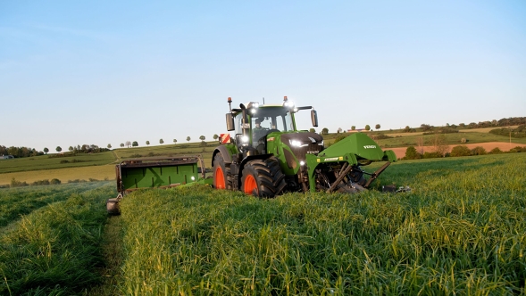 Un tractor Fendt con una combinación de Slicer segando un prado verde con un cielo azul