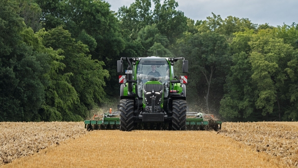 Fendt 600 Vario Un Fendt 600 Vario verde trabajando con un implemento en un campo marrón. Al fondo se ven un bosque en tono verde oscuro y un cielo nuboso.