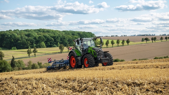 Fendt 600 Vario Un tractor Fendt verde con llantas rojas trabajando el suelo en un campo cosechado con un paisaje de montículos al fondo.