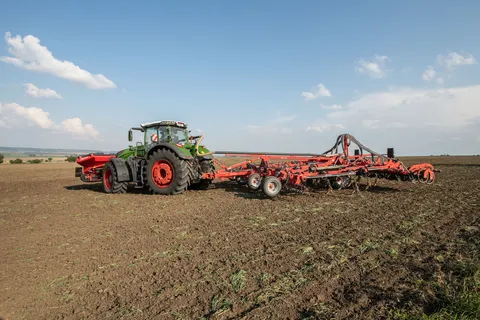 Vihreä Fendt 1000 Vario ajaa etutankin ja lautasäkeen kanssa kaarteessa pellolla.