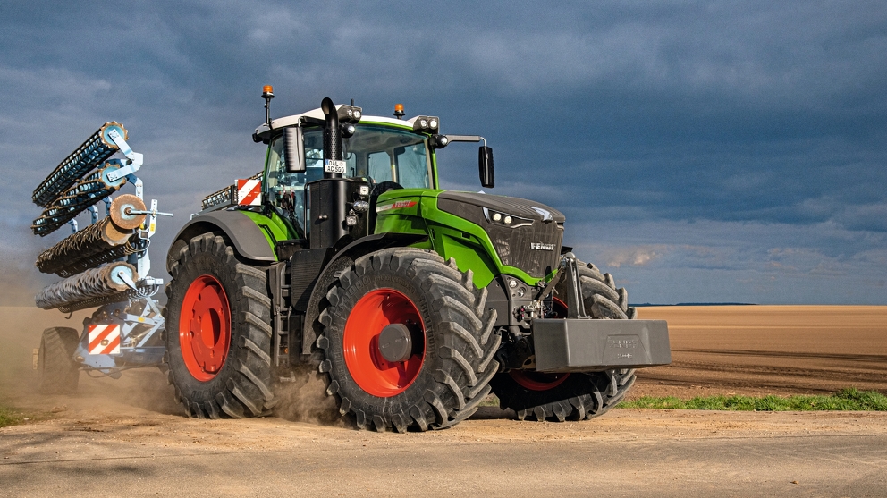 Fendt 1000 Vario ajaa työkoneen kanssa tiellä pellon vieressä.