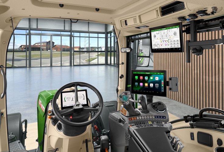 Fendt-ohjaamon sisätila Apple CarPlaylla Sisäkuva traktorin ohjaamosta kuljettajan näkökulmasta, näkyvissä ohjauspyörä, FendtONE-ohjauskyynärnoja joystickillä ja Apple CarPlay päätelaitteella sekä lisäpäätelaite katossa.
