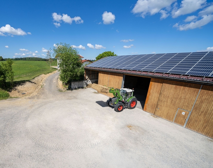 Fendt 500 Vario etukuormaajalla Vihreä Fendt 500 Vario ajaa hallista ulos etukuormaaja nostettuna ja paali mukana.