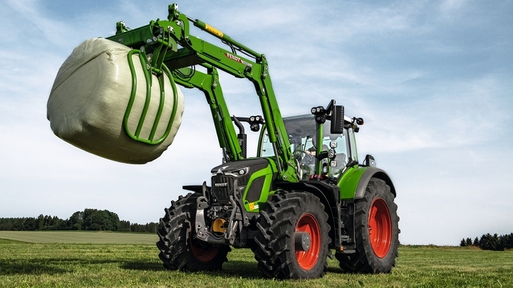 Vihreä Fendt 600 Vario seisoo vihreällä pellolla ja nostaa etukuormaajallaan valmiin pyöröpaalin