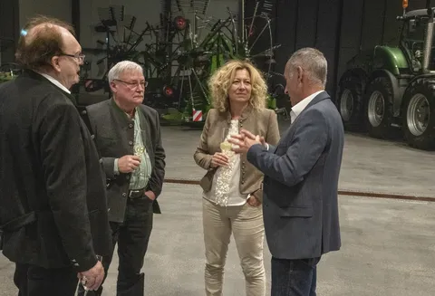 Un groupe de personnes discute lors des festivités organisées pour la création du Fendt Classic Club International dans le hall du Fendt Forum, une coupe de champagne à la main.