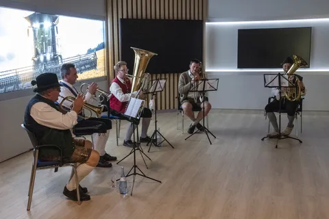 Un petit orchestre composé d'instruments à vent joue devant une image projetée d'un Fendt IDEAL Musik.