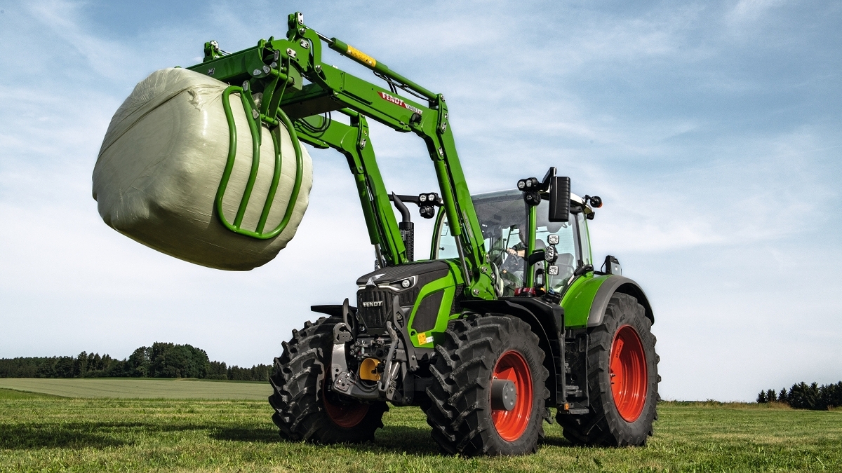 Tracteur Fendt 600 Vario Un Fendt 600 Vario avec chargeur frontal se trouve dans une prairie et porte une balle d’ensilage.