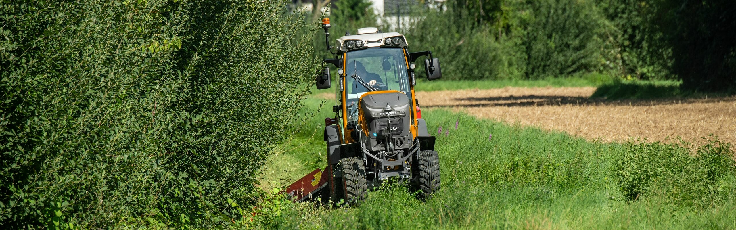 Un Fendt e100 V Vario peint en orange utilisé par les services communaux sur une bande verte