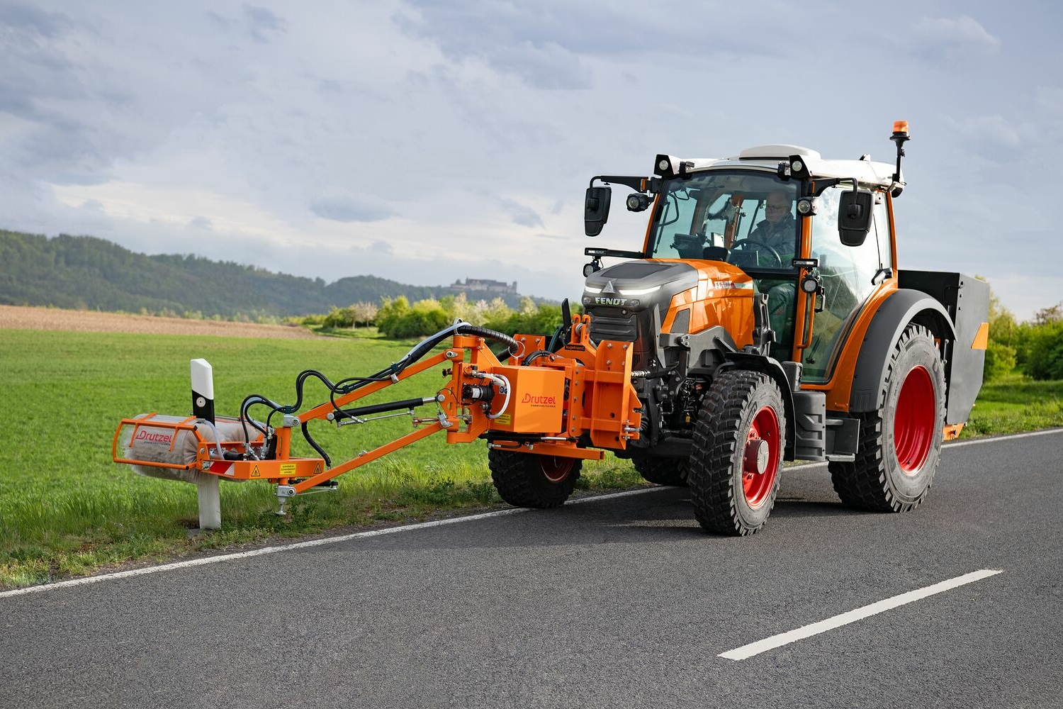 Le Fendt e100 Vario peint en orange, utilisé comme machine ISU lors d'une opération de nettoyage de pylônes sur une route départementale.