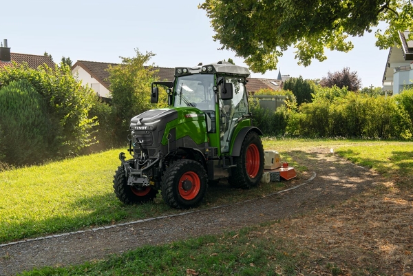 Vue d'un Fendt e100 V Vario en Nature Green avec jantes rouges à la lisière d'un village