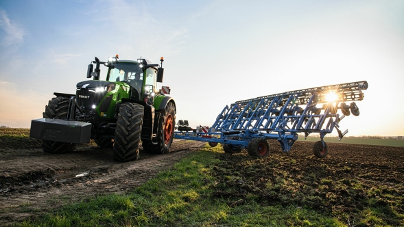 Vue frontale du Fendt 900 Vario vert avec jantes rouges et un outil porté bleu de Lemken. Le tracteur est dans un champ au crépuscule, au coucher du soleil.