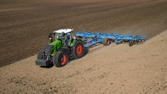 Le tracteur vert Fendt 900 Vario avec des jantes rouges et un outil porté bleu de Lemken est en action dans un champ marron.