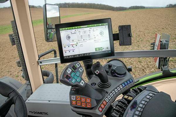 Cabine du Fendt 900 Vario Gros plan sur l’accoudoir et le terminal tactile Fendt One 12’’ dans la cabine du Fendt 900 Vario, avec vue sur un vaste champ marron.