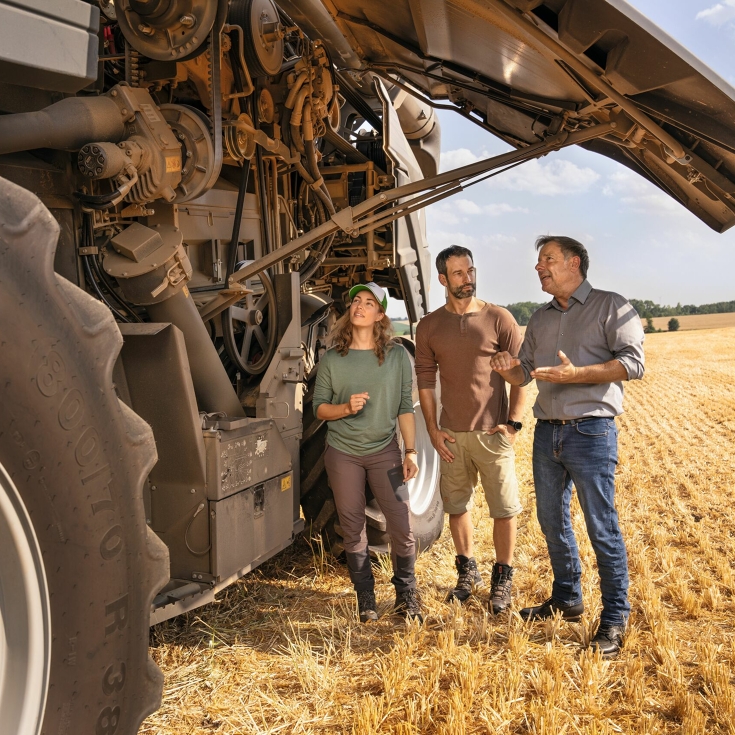 Un concessionnaire Fendt explique à un couple d'agriculteurs dans un champ comment fonctionne la moissonneuse-batteuse Fendt.