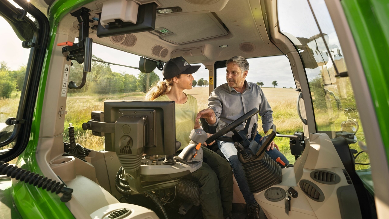 Un concessionnaire Fendt dans la cabine d’un modèle de tracteur vert de démonstration Fendt 700 Vario Gen7, chez une cliente agricultrice sur le terrain.
