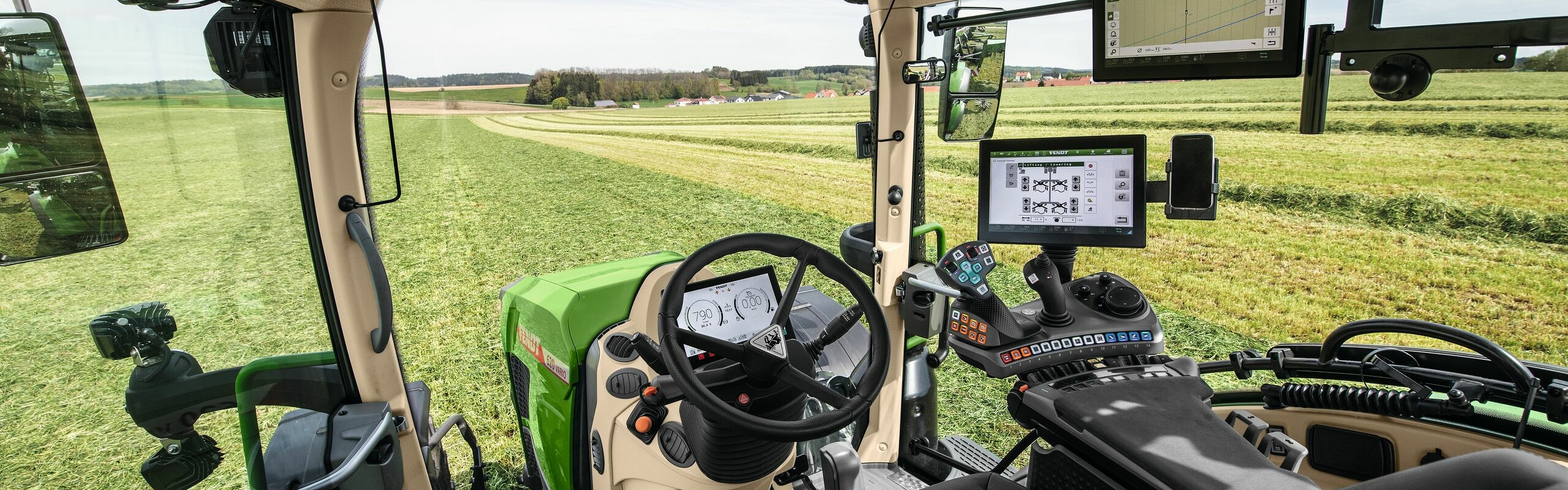 Vue intérieure de la cabine du Fendt 600 Vario avec vue sur une verte prairie.