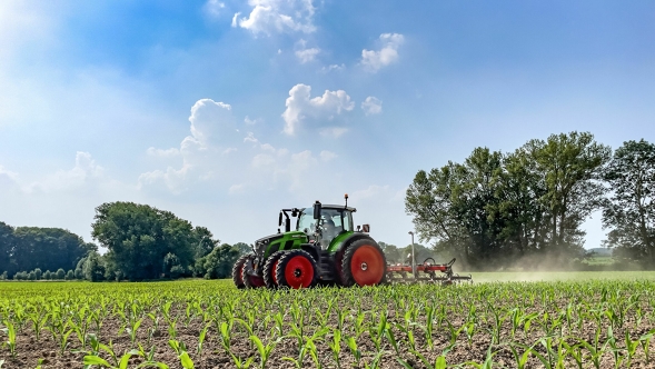 Le tracteur vert Fendt 600 Vario avec pneus jumelés en action dans un champ cultivé. En arrière-plan, on peut voir des arbres vert foncé et un ciel bleu clair avec des nuages blancs.