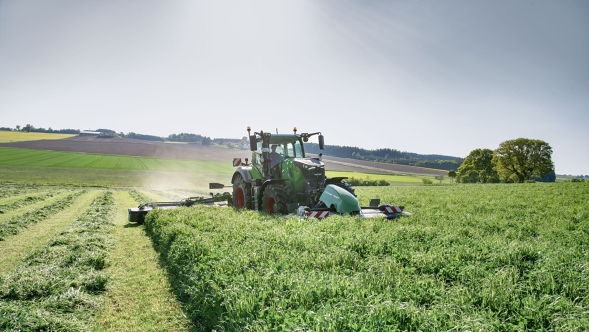 Le Fendt 700 Vario Gen7.1 lors du fauchage de prairies avec des faucheuses frontale et arrière. Un Fendt 700 Vario Gen7.1 avec faucheuse en action lors de la récolte de l'herbe sur une grande prairie verte sous un ciel dégagé.