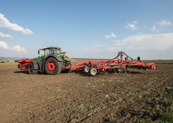 un Fendt 1000 Vario vert prend un virage sur un champ avec une trémie frontale et un pulvériseur à disques simple