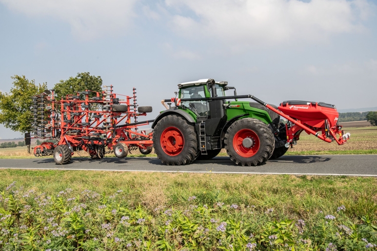 un Fendt 1000 Vario vert roule sur la route avec un outil à l’avant et un à l’arrière