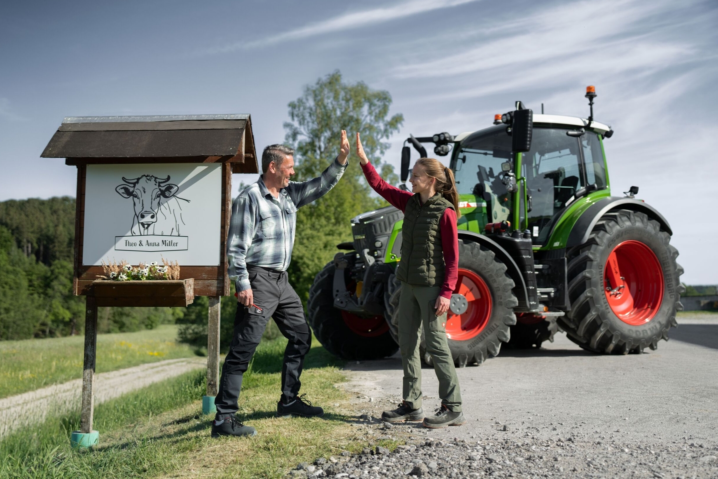 L'agriculteur et sa fille se tiennent devant le panneau de leur ferme avec leur Fendt 500 Vario en arrière-plan.