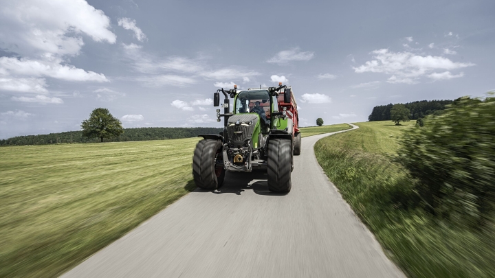 Un Fendt 700 Vario avec remorque autochargeuse roule sur une route de campagne en été