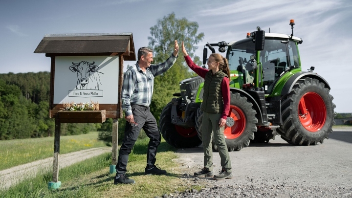 L'agriculteur et sa fille se tiennent devant le panneau de leur ferme avec leur Fendt 500 Vario en arrière-plan.