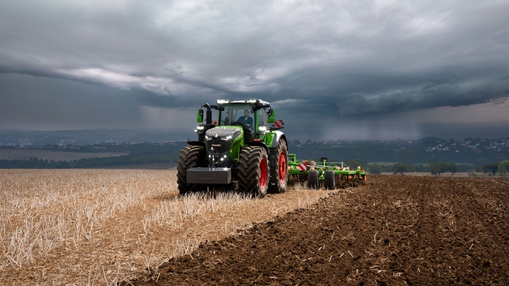 Le tracteur Fendt 1000 Vario effectue encore son travail à pleine puissance dans les champs malgré les lourds nuages d'orage qui s'approchent au loin.