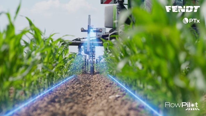 Entre les rangées de plants, on aperçoit la houe montée sur un tracteur Fendt. Le RowPilot est installé sur le dessus de la houe, la détection des rangées est indiquée par des lignes bleues tracées.