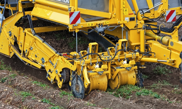 Un tracteur Fendt vert avec une arracheuse de pommes de terre ROPA déverse des pommes de terre dans un camion en bordure de champ.