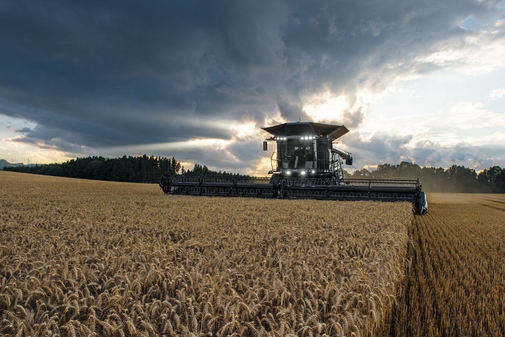 Une Fendt IDEAL en anthracite bat du blé avec un cueilleur monté dans la lumière du soir.