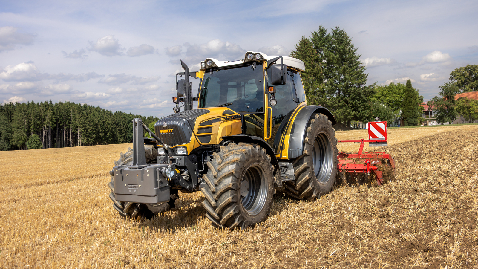 Un Fendt 200 Vario doré se trouve dans un champ, avec une forêt en arrière-plan.