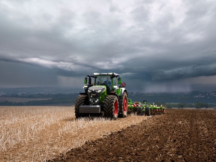 Le tracteur Fendt 1000 Vario effectue encore son travail à pleine puissance dans les champs malgré les lourds nuages d'orage qui s'approchent au loin.