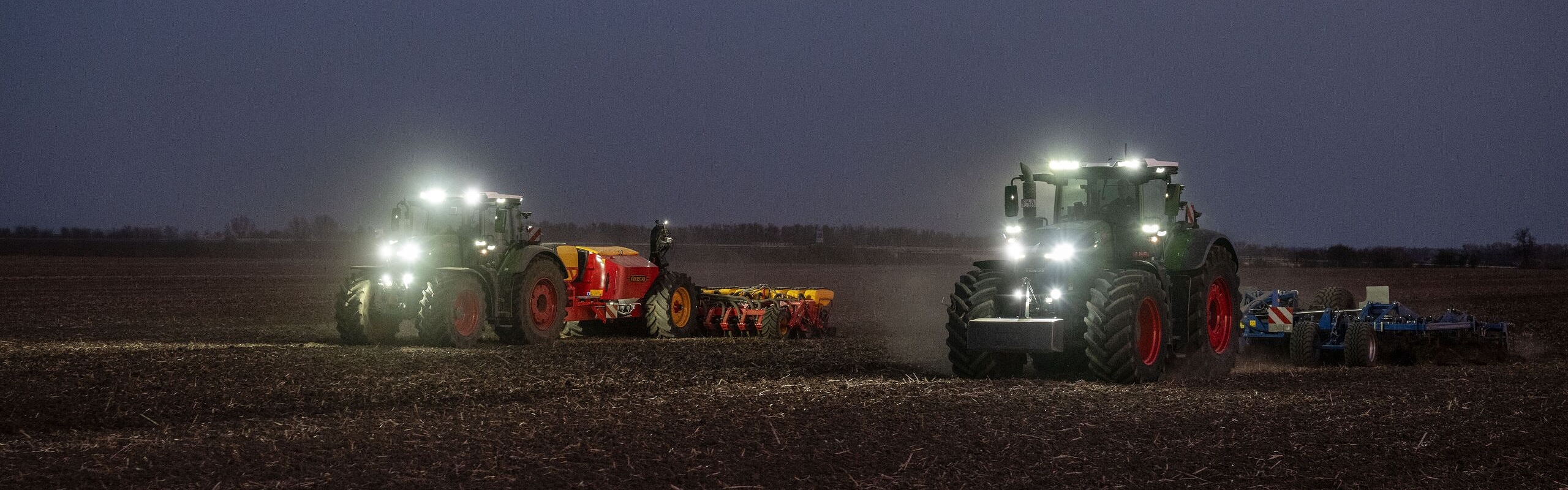 Le Fendt 1000 Vario et le Fendt 800 Vario travaillent ensemble dans l’obscurité sur un champ avec les phares allumés.