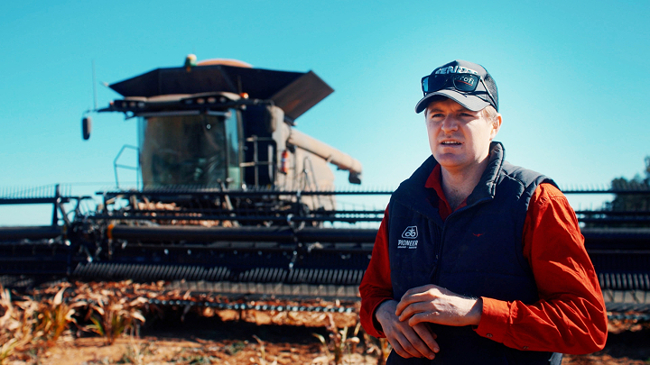 Egy farmer áll egy nagy fekete Fendt IDEAL traktor mellett egy mezőn, háttérben kék égbolttal.