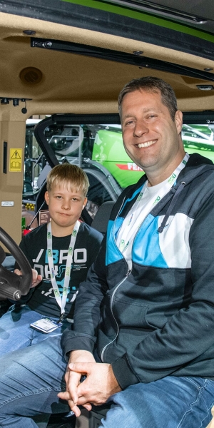 Egy kis szőke srác büszkén ül apjával egy Fendt-traktor fülkéjében.