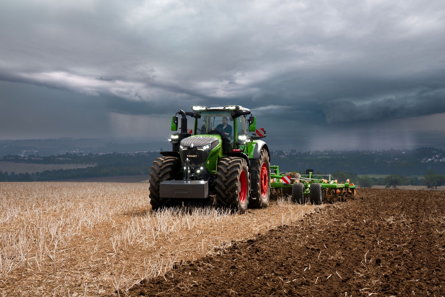 A veszélyesen gyülekező viharfelhők előtt a távolban a Fendt 1000 Vario traktor még erőteljesen végzi a terepmunkát.