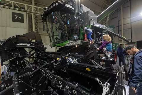 Children climb a ladder into the cab of the Fendt straw walker combine harvester
