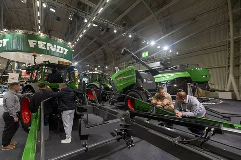 Trade fair visitors leaning on a Fendt rake, with a round baler and a Fendt combine harvester in the background