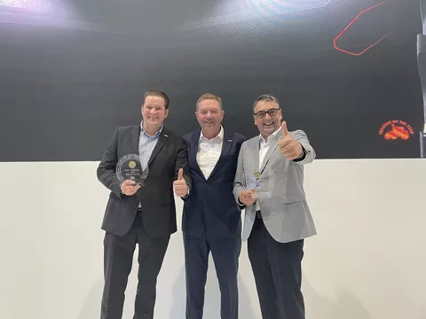 Three men stand on a stage and cheer about winning two TotY 2025 awards.