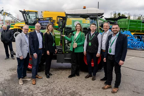 7 people, women in the centre, a woman with a green jacket holds a prize in her hand, in front of a green Fendt tractor