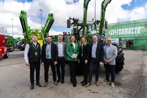 7 people, women in the centre, a woman with a green jacket holds an award in her hand, in front of a green Fendt tractor