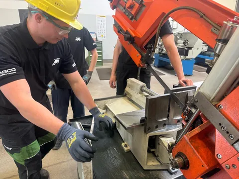 3 men (apprentices) stand at a band sawing machine and saw