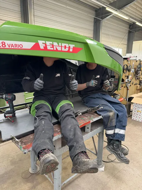 2 men (apprentices) sit under the Fendt bonnet and give a thumbs up